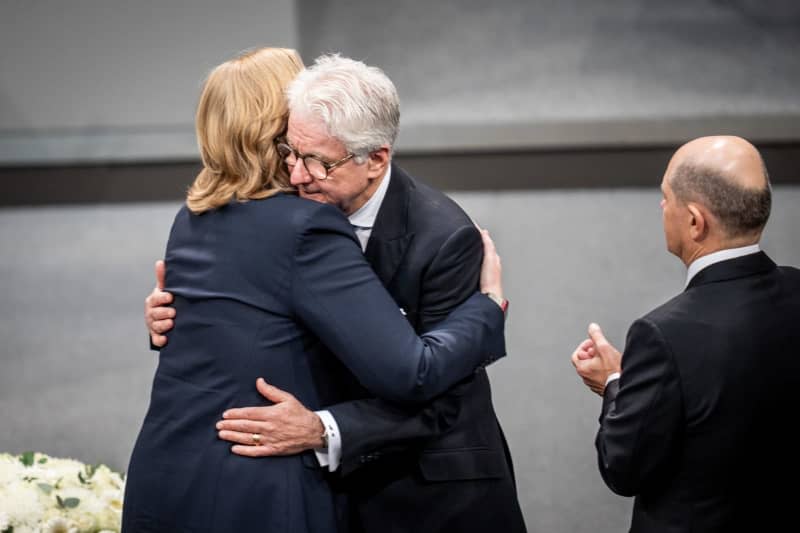 Marcel Reif, sports presenter, hugs Baerbel Bas (L), President of the German Bundestag, next to German Chancellor Olaf Scholz (R), at the German Bundestag's commemoration of the Day of Remembrance for the Victims of National Socialism after his speech. Michael Kappeler/dpa