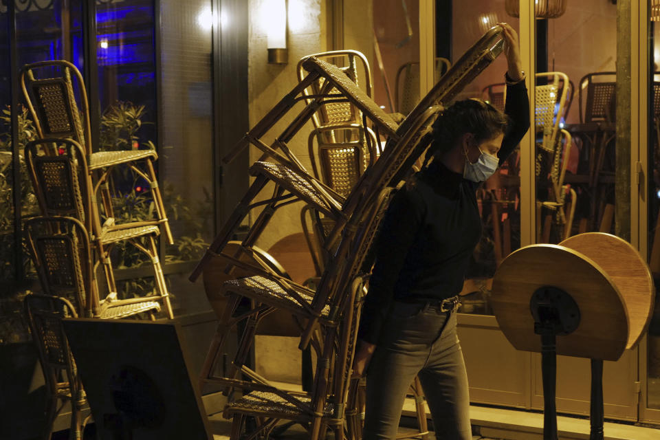 A waiter carries chairs to close a bar terrace in Paris, Monday Sept. 28, 2020. French President Emmanuel Macron justified on Monday new restrictions in the country to limit the spread of the virus as restaurant and bar owners forced to shut down expressed anger at the measures. Milder restrictions have been ordered in ten other cities including Paris, with gyms shut down, public gatherings of more than 10 people banned and bars ordered to close at 10 p.m. (AP Photo/Francois Mori)