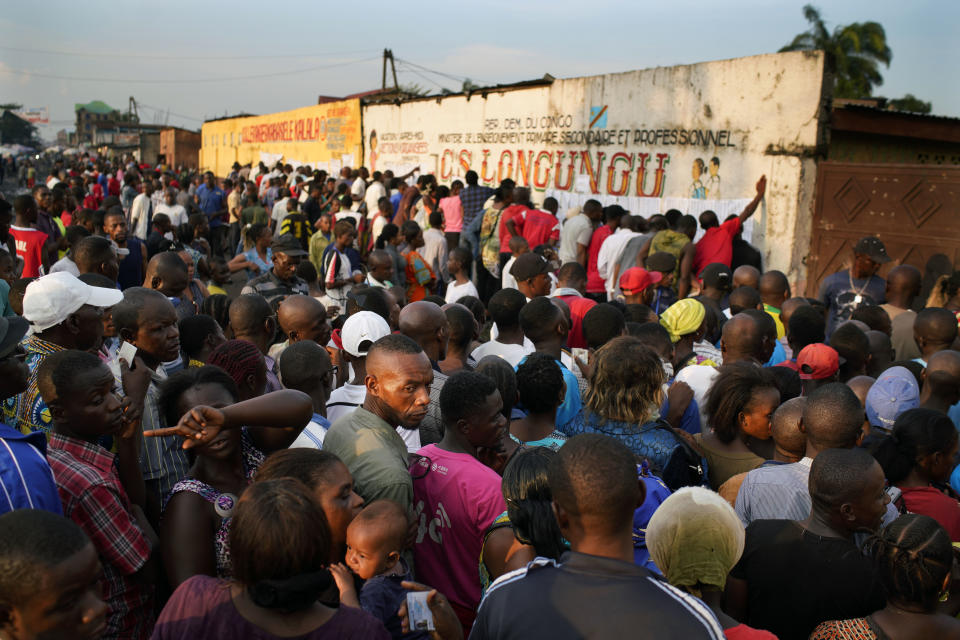 Election officials tape the voter's registrations list to the wall of the Les Anges primary school in Kinshasa, Congo, as voters start to check their names, Sunday Dec. 30, 2018. The voting process was delayed when angry voters burned six voting machines and ballots mid-day, angered by the fact that the registrations lists had not arrived. Replacement machines had to be brought in, and voting started at nightfall, 12 hours late. Forty million voters are registered for a presidential race plagued by years of delay and persistent rumors of lack of preparation. (AP Photo/Jerome Delay)