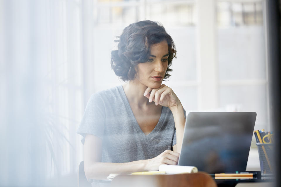 Beautiful young businesswoman with hand on chin using laptop in office