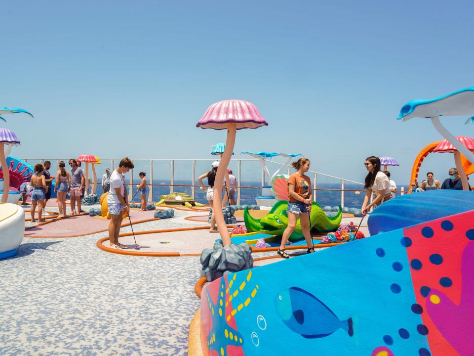 People participate in mini golf tournament onboard Wonder of the Seas with clear blue skies in the baackground