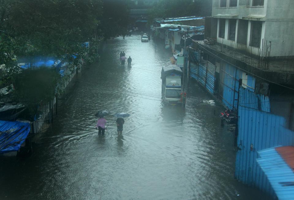 People brave knee deep water along a flooded road in Mumbai. (Photo by Arun Patil)