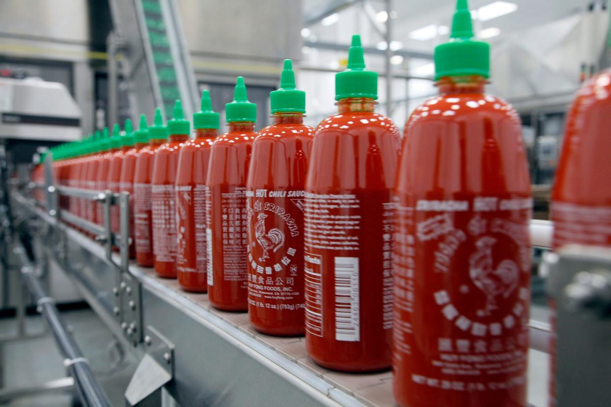 bottles of sriracha are lined up on an assembly line