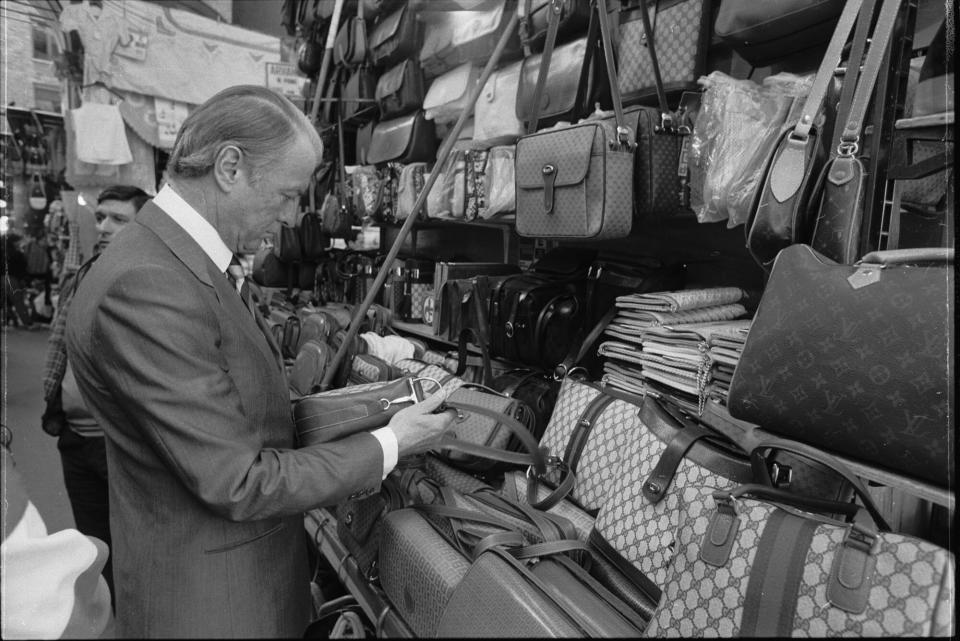 Black and white photo of fashion Designer Roberto Gucci looking at handbags