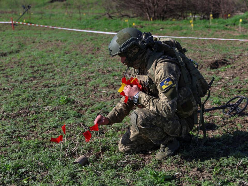 A Ukrainian military sapper places red flags next to a part of a Russian cluster bomb while demining a field in Kherson region (Reuters)