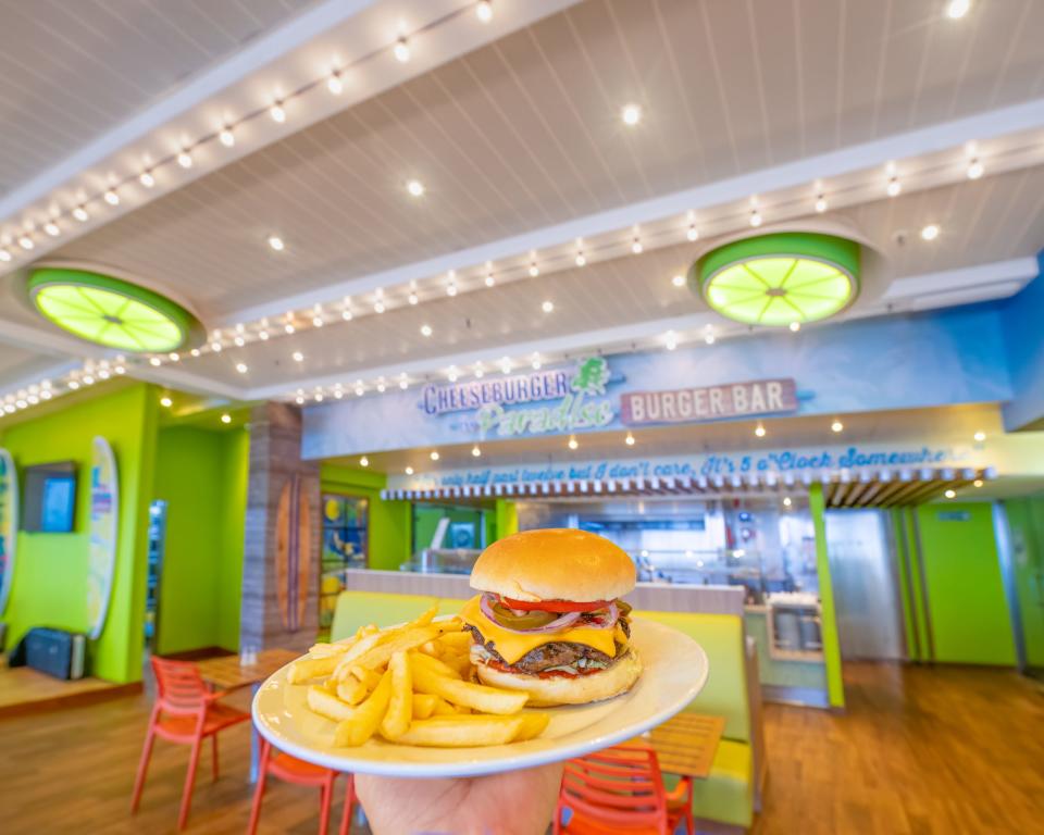 A person holding up a plate with fries and a burger on the Margaritaville at Sea Paradise