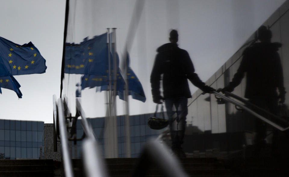 A man carries a cycling helmet and walks by EU flags as he is reflected in a marble staircase outside EU headquarters in Brussels, Wednesday, Oct. 28, 2020. This week, news struck that the European Centre for Disease Prevention and Control had recorded Belgium as having the highest 14-day cumulative number of COVID-19 cases per 100,000 citizens, just surpassing the Czech Republic. (AP Photo/Virginia Mayo)