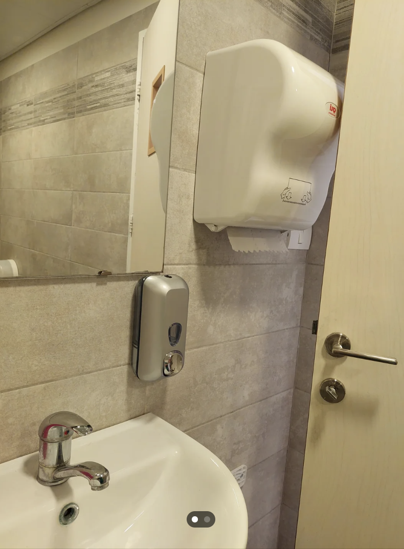 Public restroom with a sink, a soap dispenser, and a hand dryer on the wall