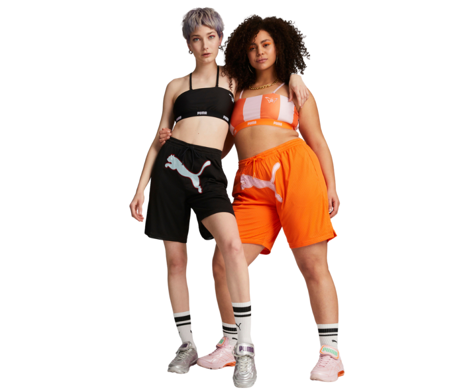 Two women model the Dua Lipa x Puma basketball short and bralette sets in orange and black