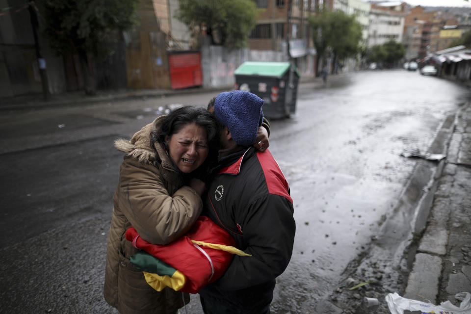 A couple, holding a Bolivian flag, embrace after spending the night celebrating the resignation of President Evo Morales in La Paz, Bolivia, Monday, Nov. 11, 2019. Morales resigned Sunday under mounting pressure from the military and the public after his re-election victory triggered weeks of fraud allegations and deadly protests.(AP Photo/Natacha Pisarenko)