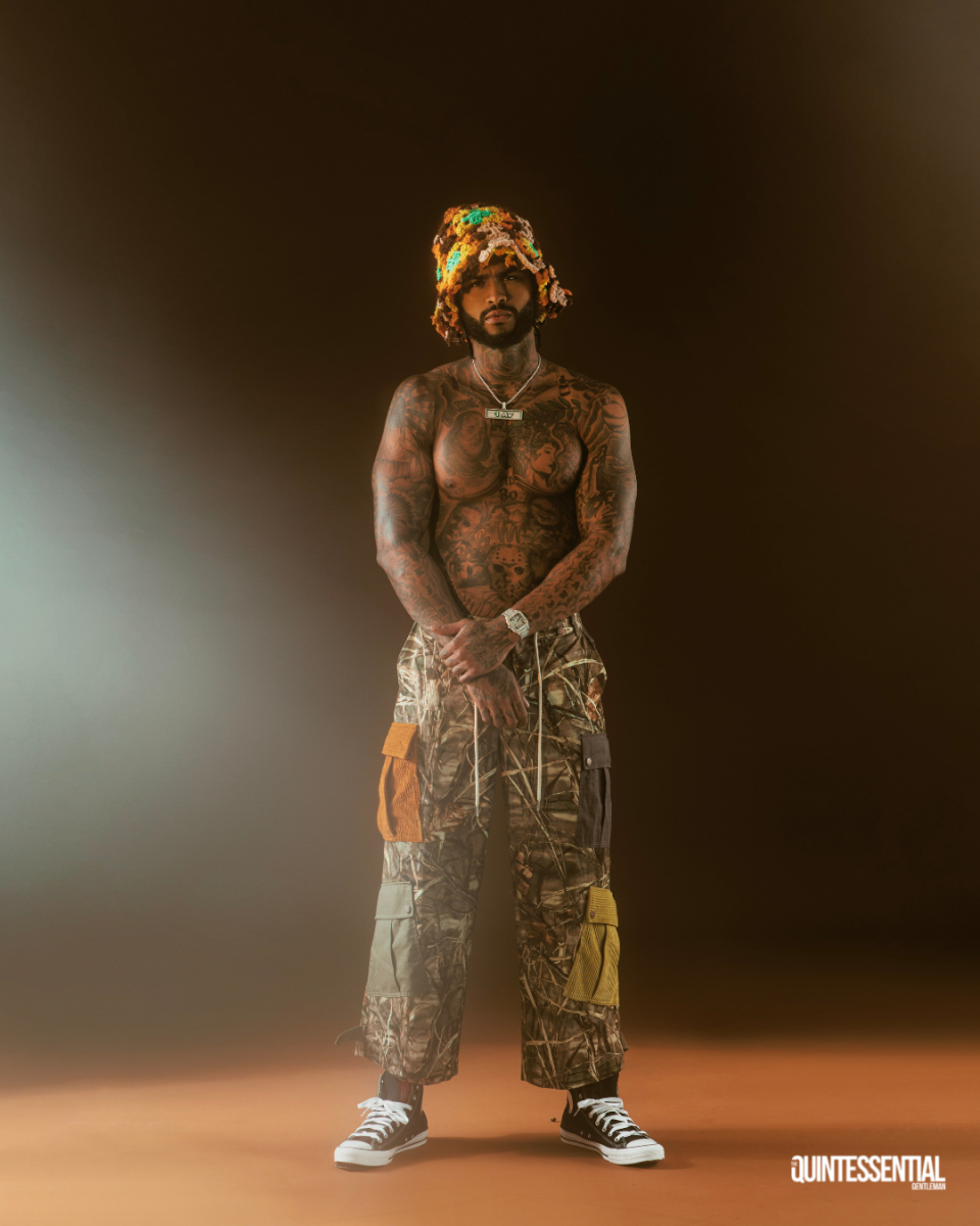 Dave East in The Quintessential Gentleman 2022 October style issue wearing nature-print cargo pants, crotchet bucket hat and no shirt.