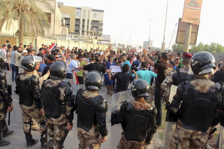 Iraqi security forces stand in front of people demonstrating against power cuts amid an intense heatwave and protesting what they call corruption and poor services, in Amara, southeast of Baghdad, August 4, 2015. REUTERS/Essam Al-Sudani