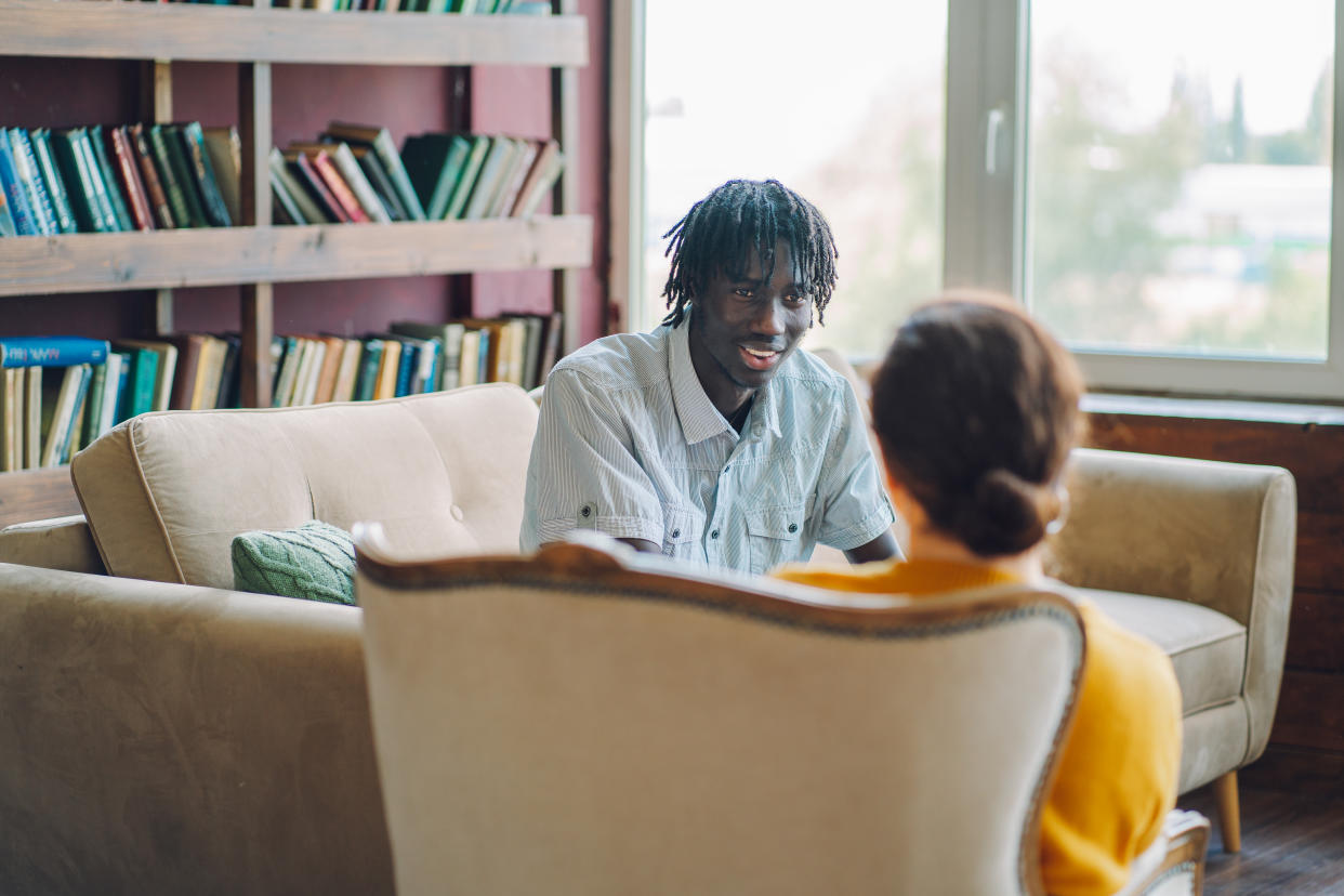 Young man in therapy. A young man sit on a sofa in a therapist office against female counselor