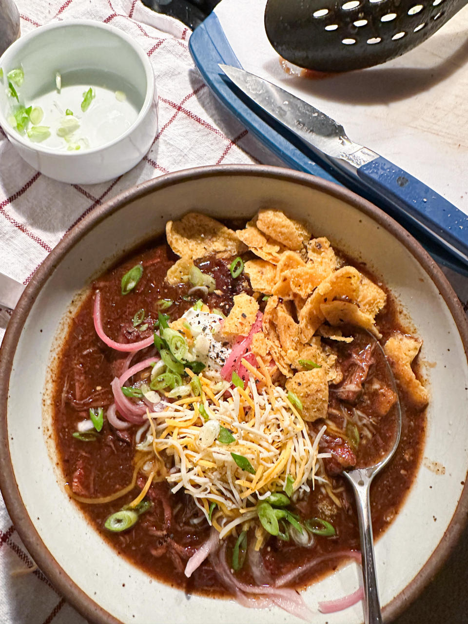 Bowl of chili garnished with shredded cheese fritos and onions