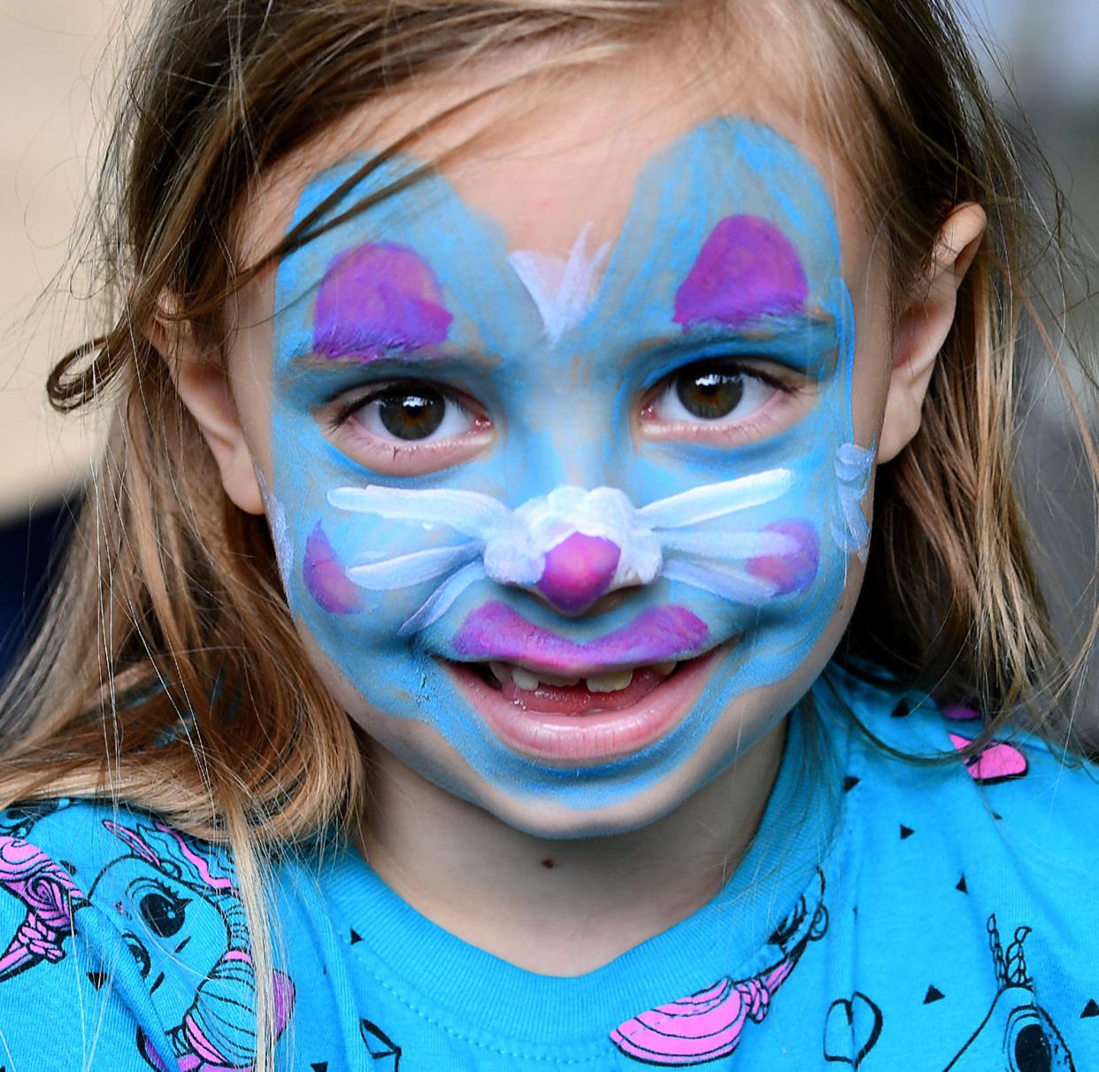 Zoe Herbert, 6, of Grafton, smiles after getting her face painted by Maggie Mussler, 17, to look like a blue bunny at the Apple Tree Arts face painting booth during the Grafton Farmers Market at the Grafton Municipal Town Building on 30 Providence Road.
