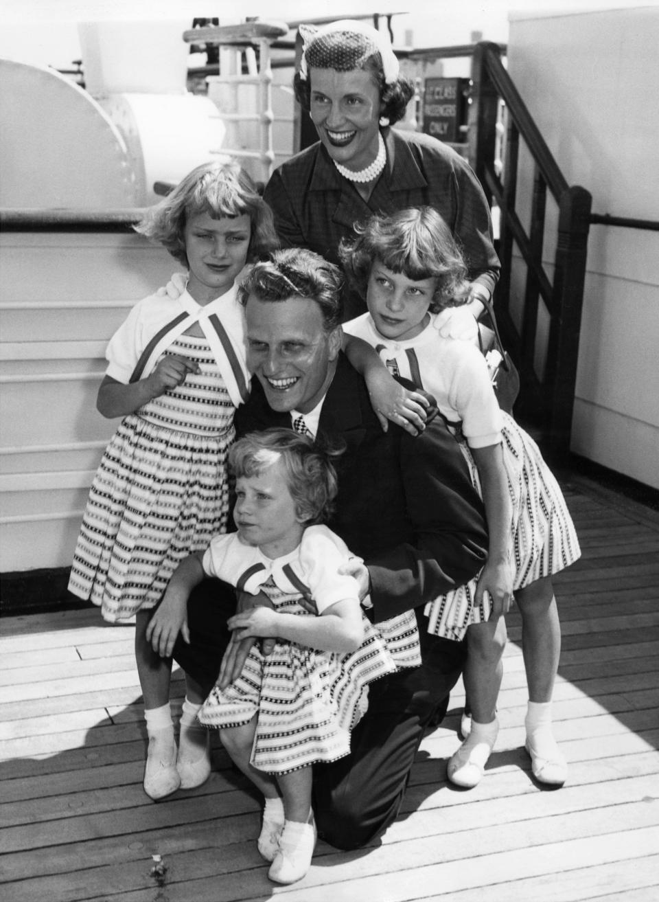 NEW YORK, UNITED STATES:  Billy Graham, 35, the American evangelist, is greeted by his wife and children, Virginia, 8 (L), Anne, 6 (R) and Ruth (Bunny), 3 (foreground) aboard the liner 'Queen Mary' on his return to New York 07 June 1954 from a religious tour of Europe. Graham, (son of a dairy farmer, born in 1918 in Charlotte, NC), attended Florida Bible Institute and was ordained a Southern Baptist minister in 1939 and quickly gained a reputation as a preacher. During the 1950s he conducted a series of highly organized revivalist campaigns in the USA and UK, and later in South America, the USSR and Western Europe. (Photo credit should read AFP/AFP/Getty Images)