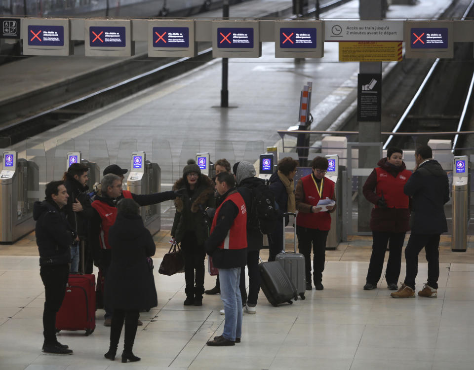 Railway employees, with red jackets, give informations to travellers at the Gare de Lyon train station, Friday, Dec. 6, 2019 in Paris. Frustrated travelers are meeting transportation chaos around France for a second day, as unions dig in for what they hope is a protracted strike against government plans to redesign the national retirement system. (AP Photo/Rafael Yaghobzadeh)
