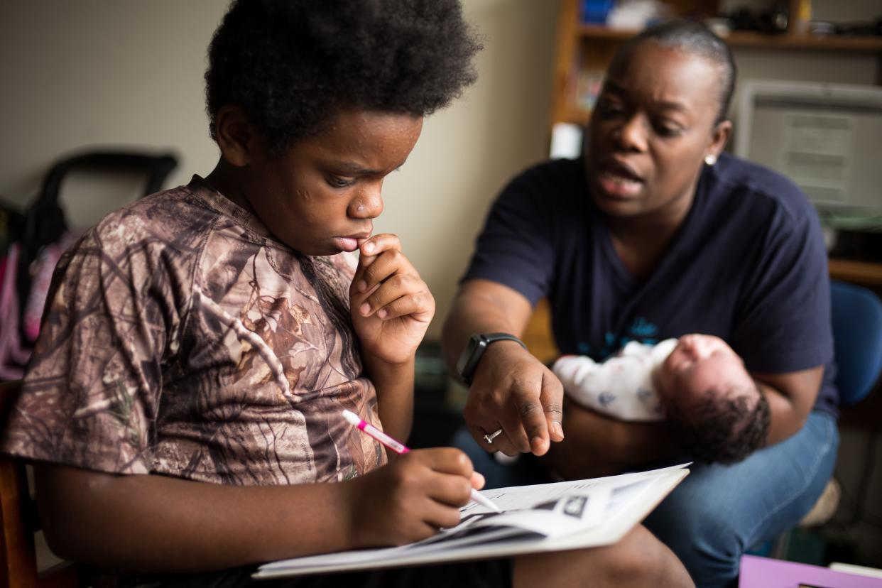 Malik Gordon gets assistance from his mother, Victoria Gordon, while she holds her 3-week-old nephew, Elijah Gordon, at their home in Nashville, Tenn., Wednesday, Sept. 16, 2020. Malik, a sixth grader at Nashville Classical Charter School, continues to adapt to the challenges of remote learning with the assistance of his mother. 