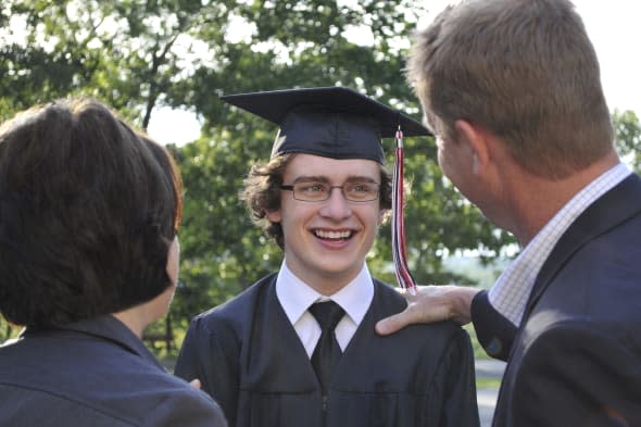 horizontal image of an excited  young graduate being congratulated by his parents. focus is on the graduate; the parents (in the