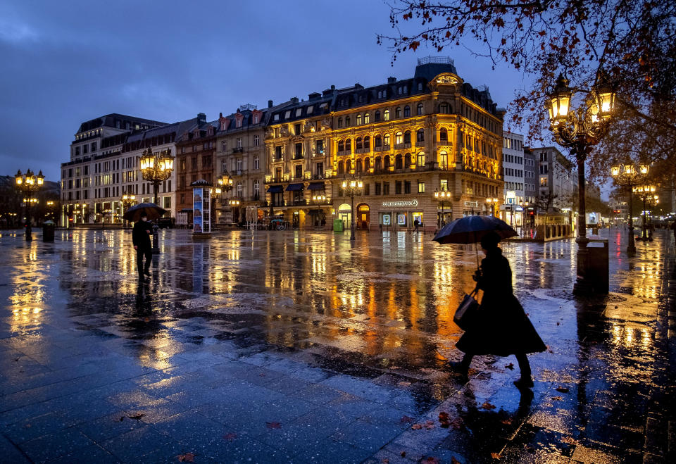 FILE - In this Jan. 22, 2021, file photo, people under umbrellas on the square in front of the Old Opera in Frankfurt, Germany, on a rainy. Nearly a year to the day after Wuhan went into lockdown to contain a virus that had already escaped, President Joe Biden began putting into effect a new war plan for fighting the outbreak in the United States, Germany topped 50,000 deaths, and Britain closed in on 100,000. (AP Photo/Michael Probst, File)