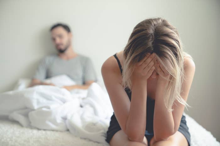 Frustrated sad girlfriend siting on a bed with her head in her hands