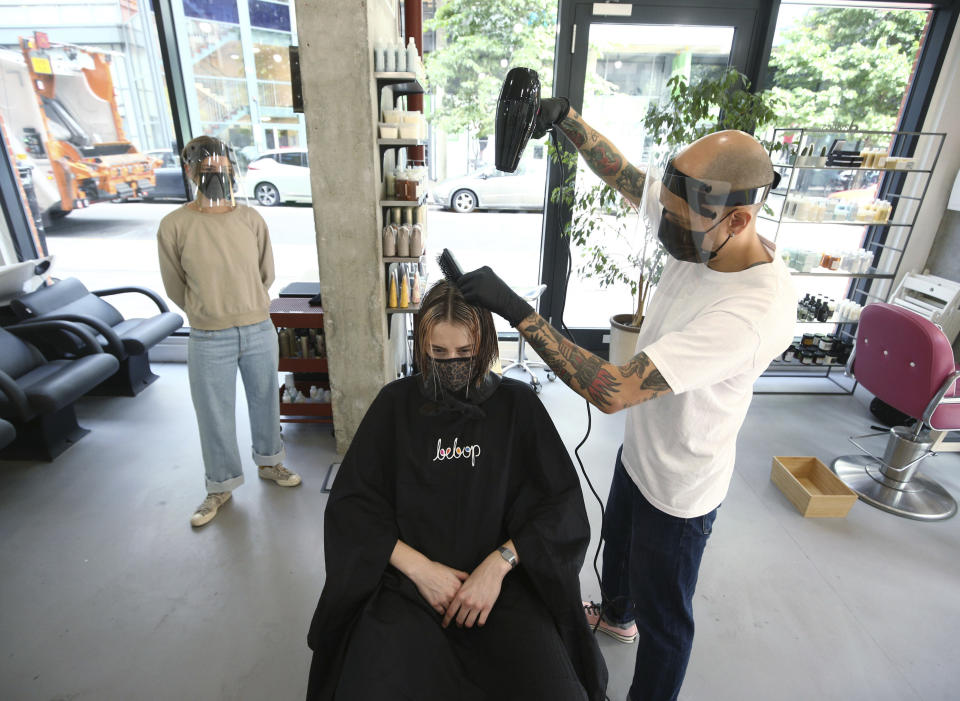 Pont Smith, co-owner and stylist of bebop hair salon in London, wears PPE as he cuts the hair of model Daisy George, as co-owner and fellow stylist Chloe Herve looks on, during final preparations ahead of the salon's reopening, as further coronavirus lockdown restrictions are lifted in the country, in London, Friday July 3, 2020. (Yui Mok/PAvia AP)