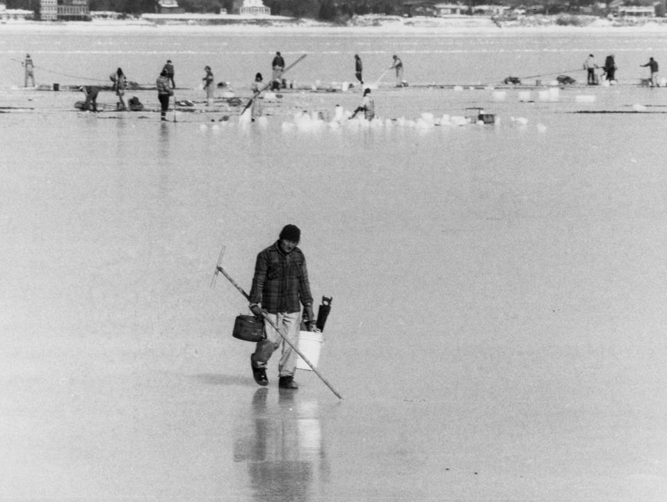 A quahogger walks across frozen Greenwich Bay in January 1982 after cutting a hole in the ice to dig for his catch.