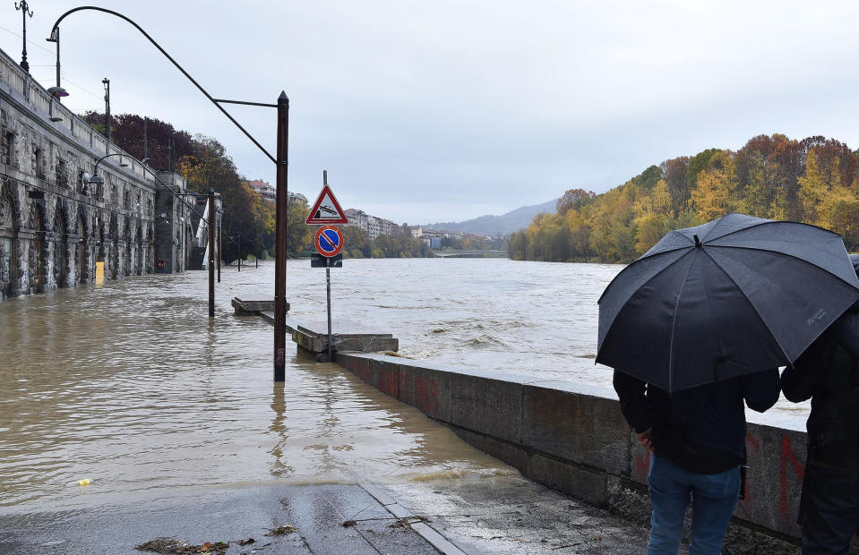 People stand under an umbrella as they look at the levels of an overflowing river Po, in the Murazzi area of Turin, northern Italy, Sunday, Nov. 24, 2019. Heavy rains and bad weather have been hitting most of Italy, causing river areas to flood and isolate hamlets in most part of northern Italy. (Alessandro Di Marco/ANSA via AP)