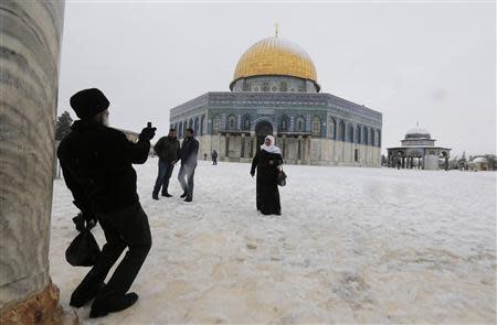 People have their pictures taken as snow falls in front of the Dome of the Rock in the compound known to Muslims as Noble Sanctuary and to Jews as Temple Mount, in winter in Jerusalem's Old City December 12, 2013. REUTERS/Ammar Awad