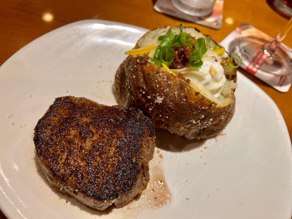 A piece of steak next to a loaded baked potato of the same size on a white plate at Outback Steakhouse