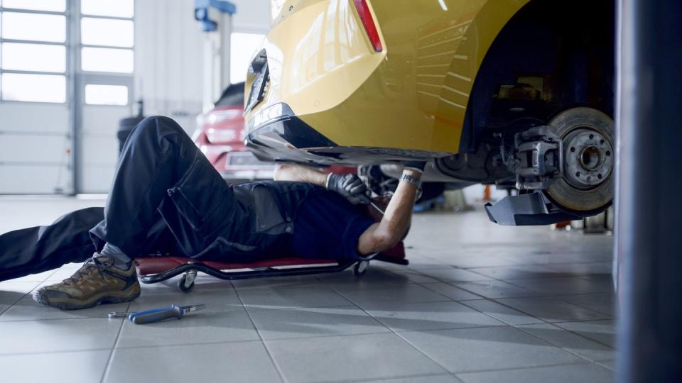 male mechanic on creeper working under car at workshop