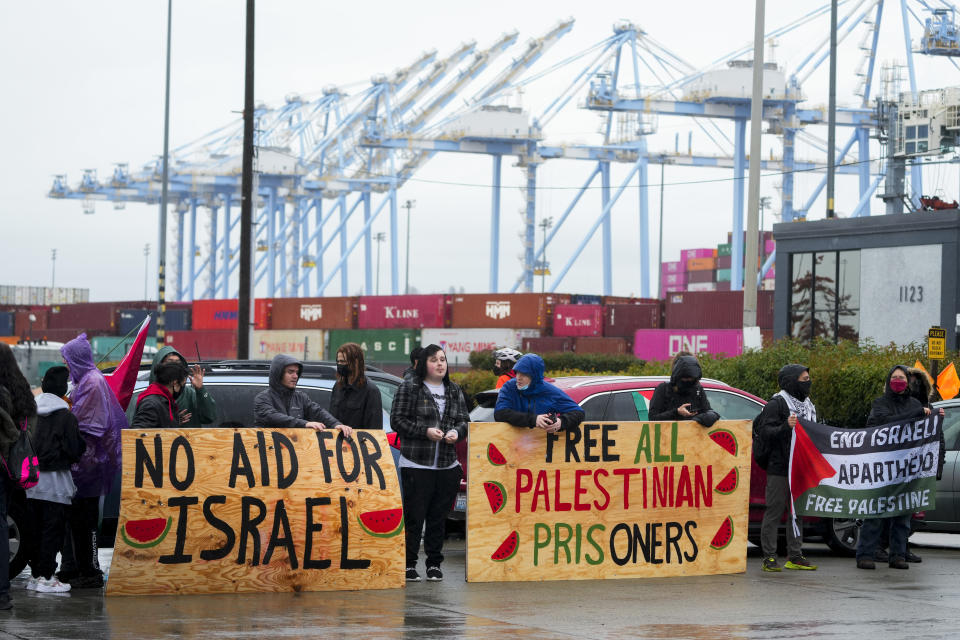 Protesters hold up large wooden signs as they block the main Port of Tacoma entrance to delay the loading of the Cape Orlando vessel, Monday, Nov. 6, 2023, in Tacoma, Wash. (AP Photo/Lindsey Wasson)