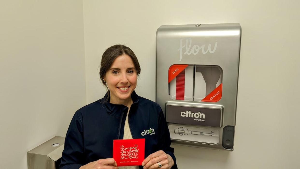 Krista Plewes, marketing director of Citron Hygiene, stands next to one of the Aunt Flow dispensers that her company supplies across Canada. The dispensers offer free tampons and menstrual pads.  (Citron Hygiene - image credit)