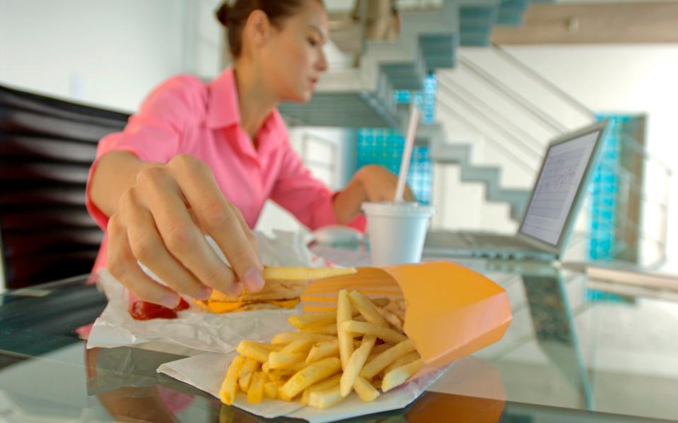 Businesswoman eating French fries, using laptop - A. Chederros