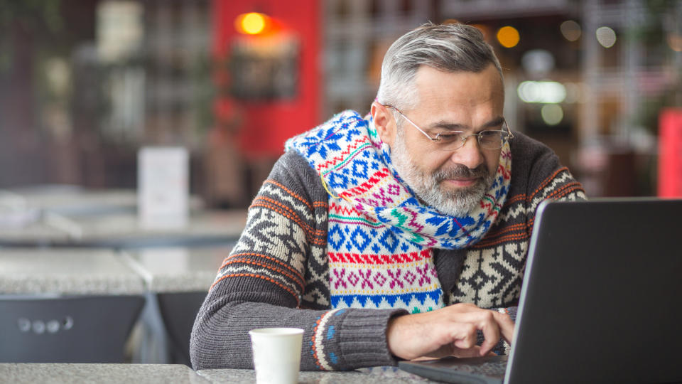 Man wearing autumn or winter clothes, scarf sitting in a cafe working using laptop