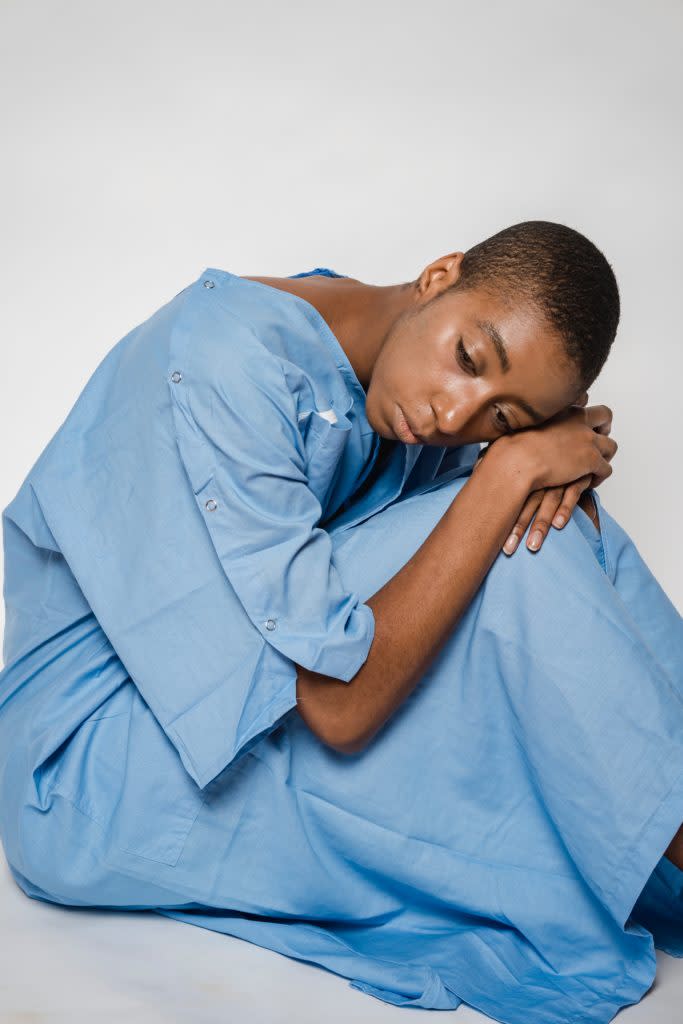 Sad Black woman in a medical gown sitting with her head down