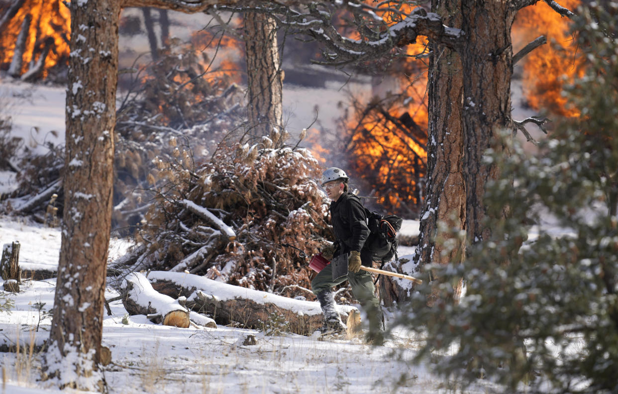 Mile High Youth Corps member John Knudsen prepares to set fire to a pile of tree debris alongside U.S. Forest Service firefighters near the Bridge Crossing picnic grounds in Hatch Gulch Wednesday, Feb. 23, 2022, near Deckers, Colo. In Colorado, climate change means snow is not always on the ground when needed so that crews can safely burn off debris piles and vegetation to help keep future wildfires from becoming catastrophic. (AP Photo/David Zalubowski)