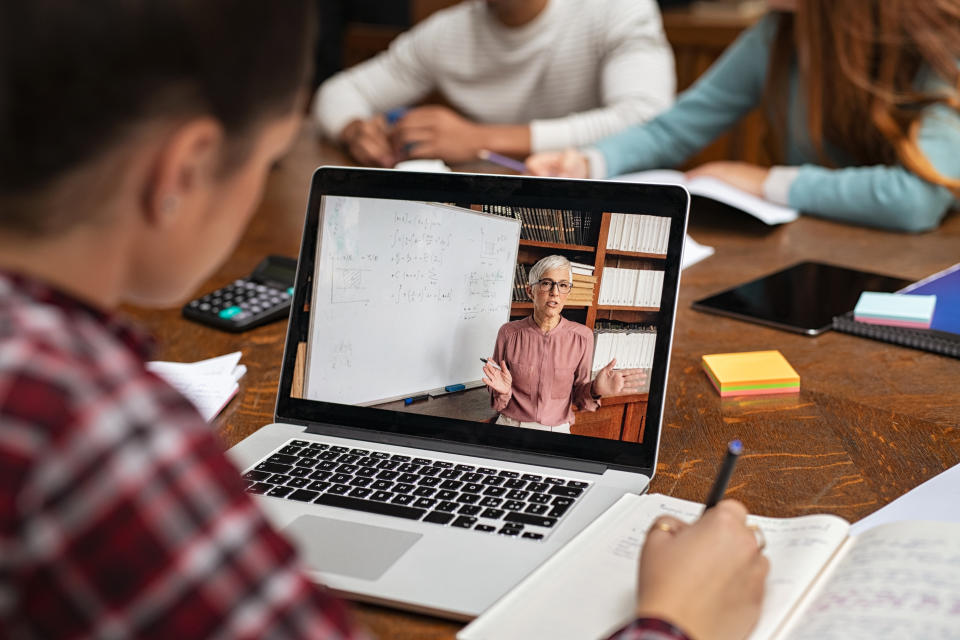 Teacher explaining lesson in video call while girl taking notes. Rear view of university student understanding concepts online while making notes. Young woman studying on computer and writing on notebook sitting in college library.