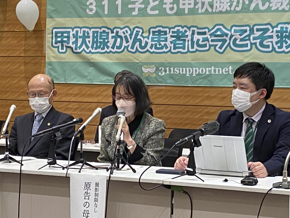 The mother of one of six plaintiffs, center, speaks during a news conference with lawyers after filing their lawsuit at the Tokyo District Court Thursday, Jan. 27, 2022, regarding six people who developed thyroid cancer being connected to the radiation leaked from the Fukushima nuclear power plant accident caused by 2014 the earthquake tsunami. Poster in rear reads "support now for thyroid cancer patients." (AP Photo/Mari Yamaguchi)