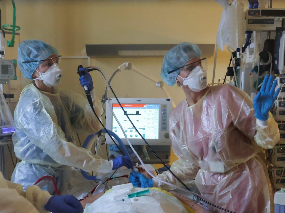 three medical staff in protective plastic suits masks operate machine and tubes connected to a patient lying flat