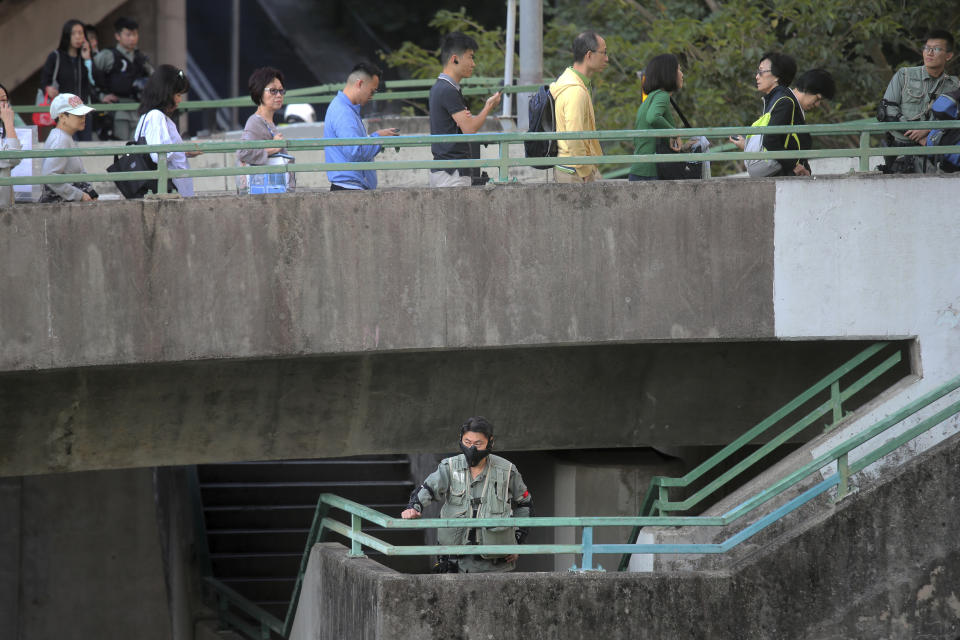 A riot policeman stands as voters line up outside of a polling place in Hong Kong, Sunday, Nov. 24, 2019. Voting was underway Sunday in Hong Kong elections that have become a barometer of public support for anti-government protests now in their sixth month. (AP Photo/Kin Cheung)