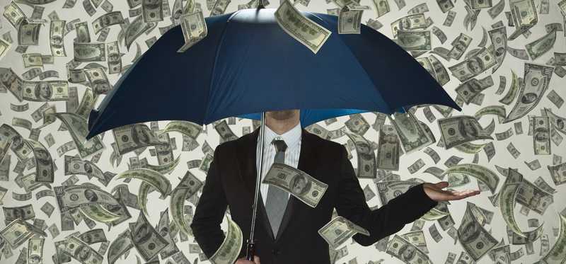 Businessman holding umbrella as money rains down.