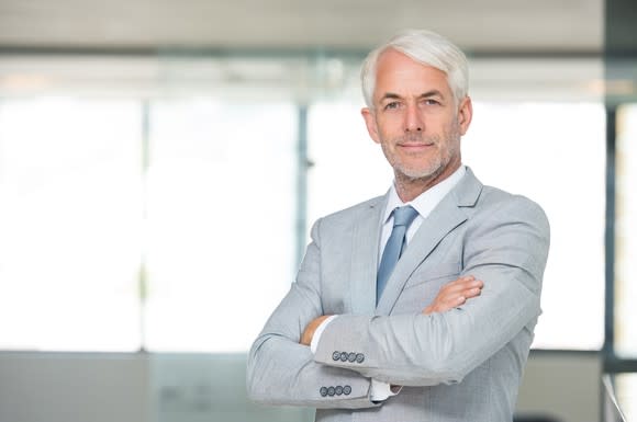 A smiling older man in a suit with his arms crossed.