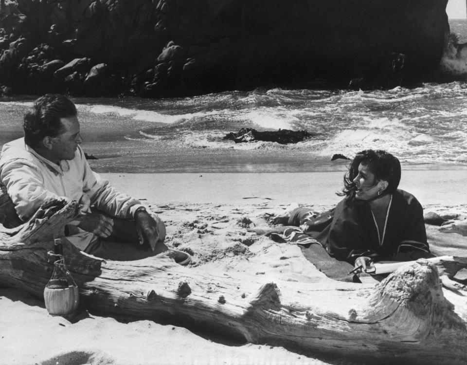 <p>Elizabeth Taylor and husband Richard Burton relax in the sand while they film <em>The Sandpiper</em> in 1965.</p>