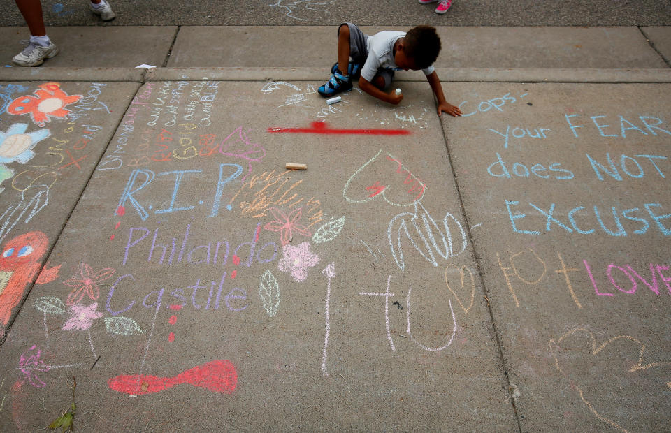 A boy sits near messages written in chalk as demonstrators protesting the shooting death of Philando Castile gather in front of the police department in St Anthony, Minnesota, on July 10, 2016.