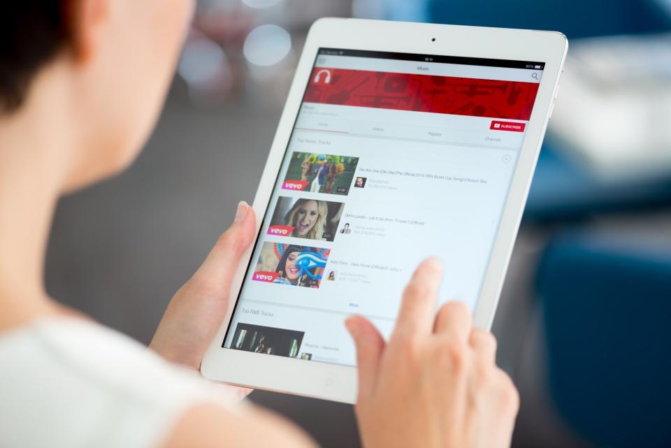 Kiev, Ukraine - May 21, 2014: Woman holding a brand new Apple iPad Air and looking on  YouTube music playlist on a screen. YouTu