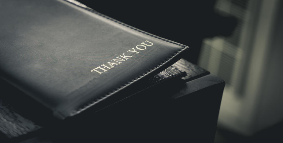 A closed book with "THANK YOU" imprinted on the cover, resting on an edge in dim lighting