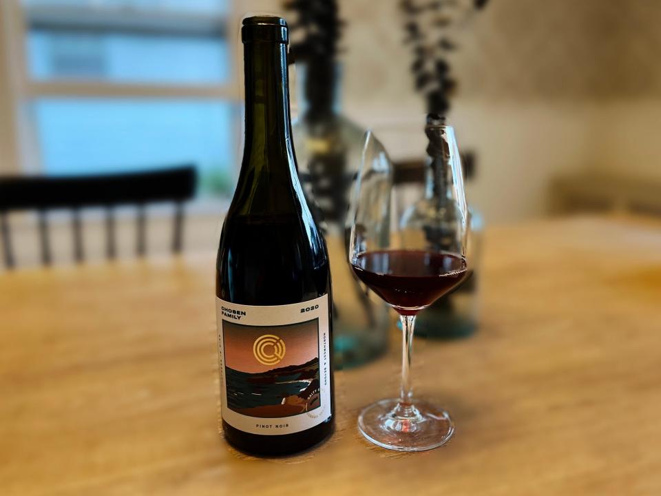 A bottle of Chosen Family Pinot Noir sits next to a partially filled glass on a table.