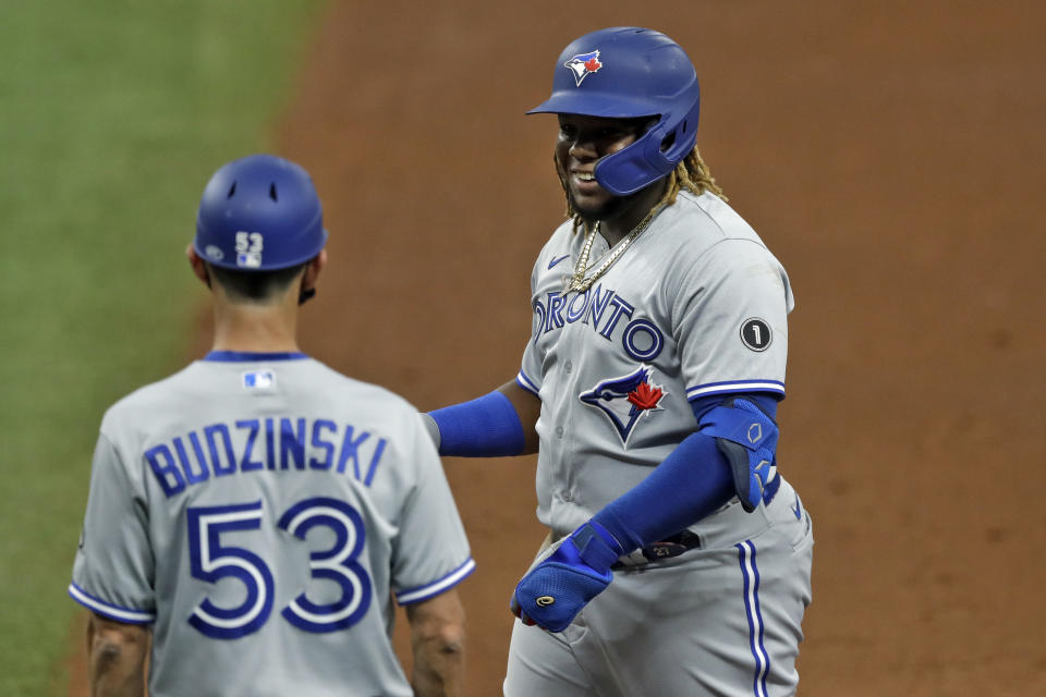 Toronto Blue Jays' Vladimir Guerrero Jr. smiles with first base coach Mark Budzinski (53) after his single off Tampa Bay Rays pitcher Ryan Yarbrough during the sixth inning of a baseball game Saturday, July 25, 2020, in St. Petersburg, Fla. (AP Photo/Chris O'Meara)