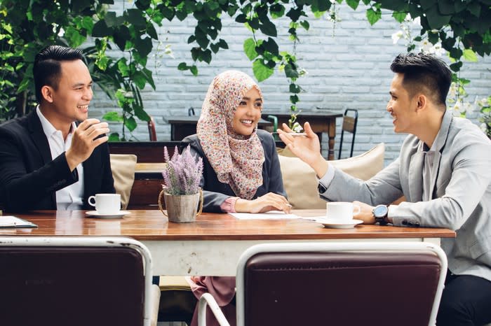 Two men and a woman sitting at a table and smiling